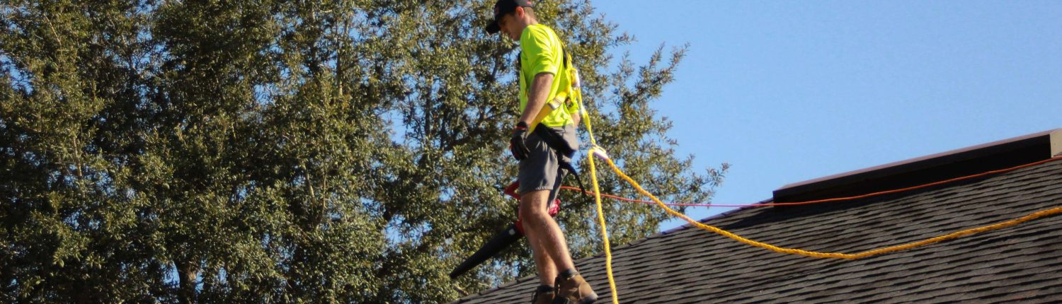 A man on the roof of a house with a hose.