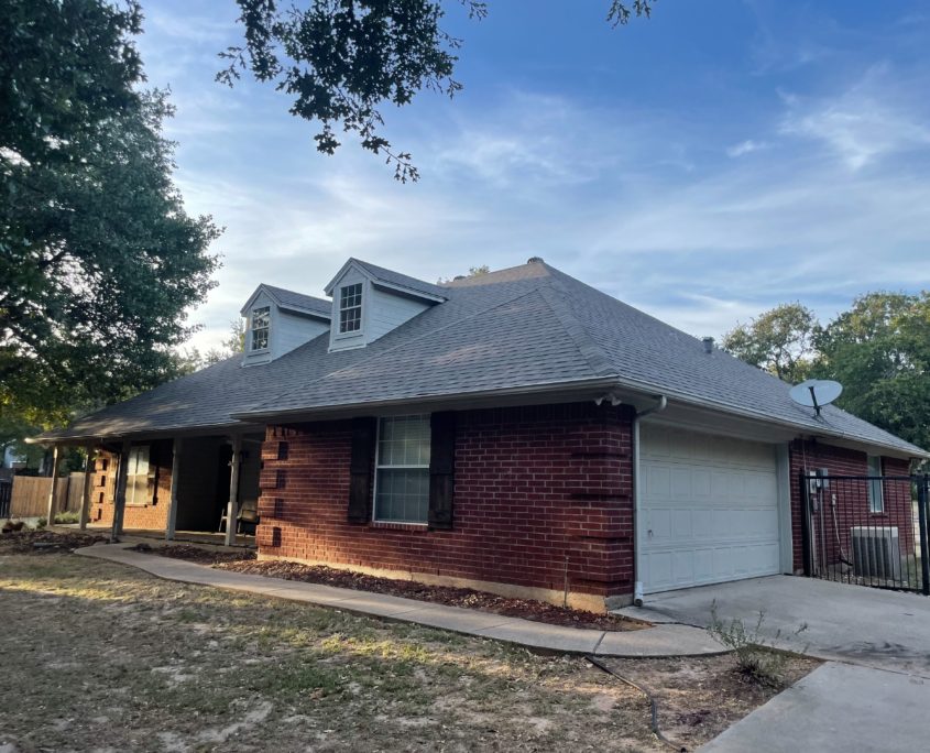 Single-story brick house with residential roofing, white garage door, and landscaped yard, under a clear sky at dusk.