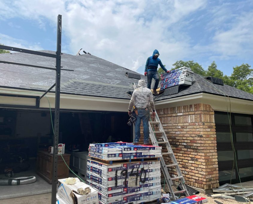 Two workers engaged in residential roofing; one on the roof and another on a ladder, with roofing materials scattered around.