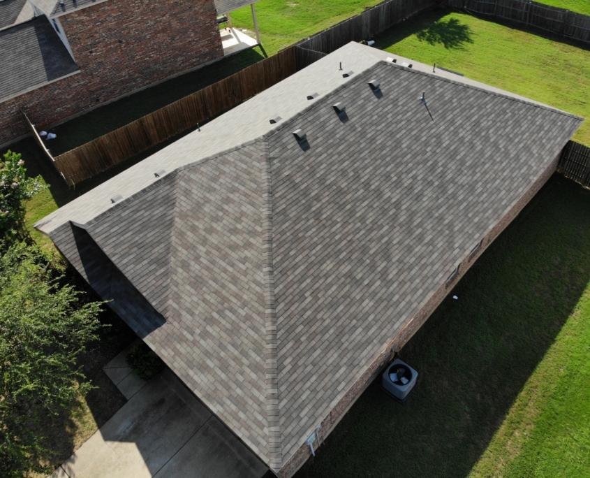 Aerial view of a large residential home with residential roofing, surrounded by a wooden fence and green grass in a suburban area.