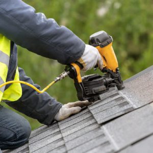 A person with a yellow vest and gloves on working on the roof of a house.