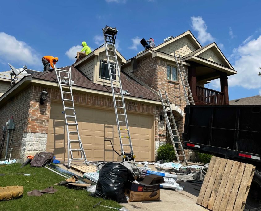 Workers on ladders performing residential roofing, installing a new roof on a suburban house, with construction debris and materials scattered around the driveway.